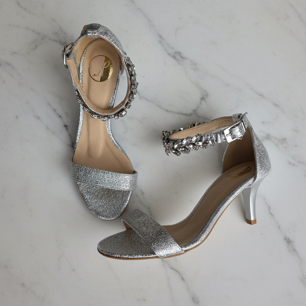Silver high-heeled shoes with embellishments on a marble surface