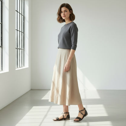 Woman wearing a gray sweater and beige skirt in a bright room with large windows.