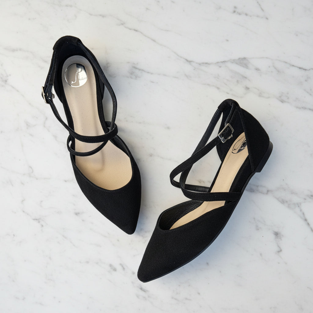 Black pointed-toe shoes with ankle straps on a white mat.
