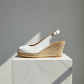 White wedge sandal with a brown sole on a marble pedestal against a gray background