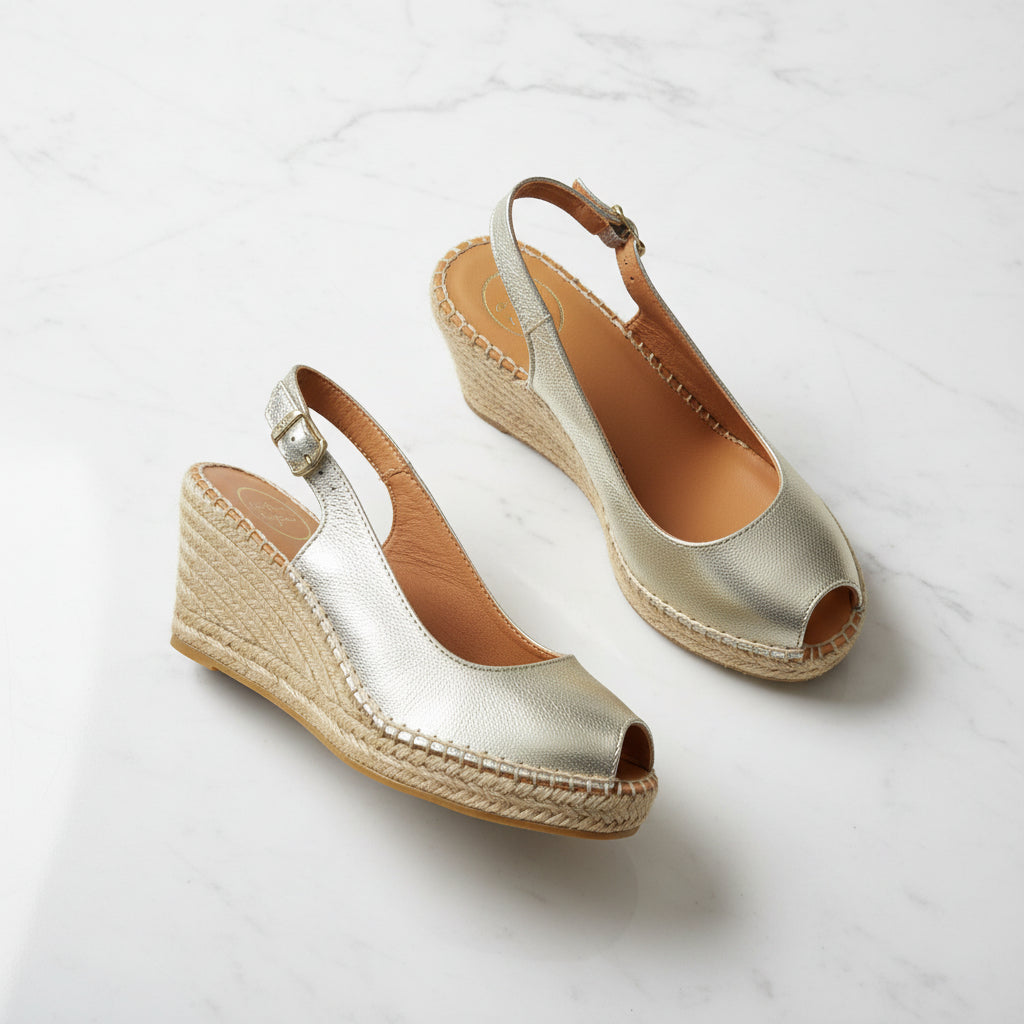 Gold wedge sandals with espadrille soles on a light gray background