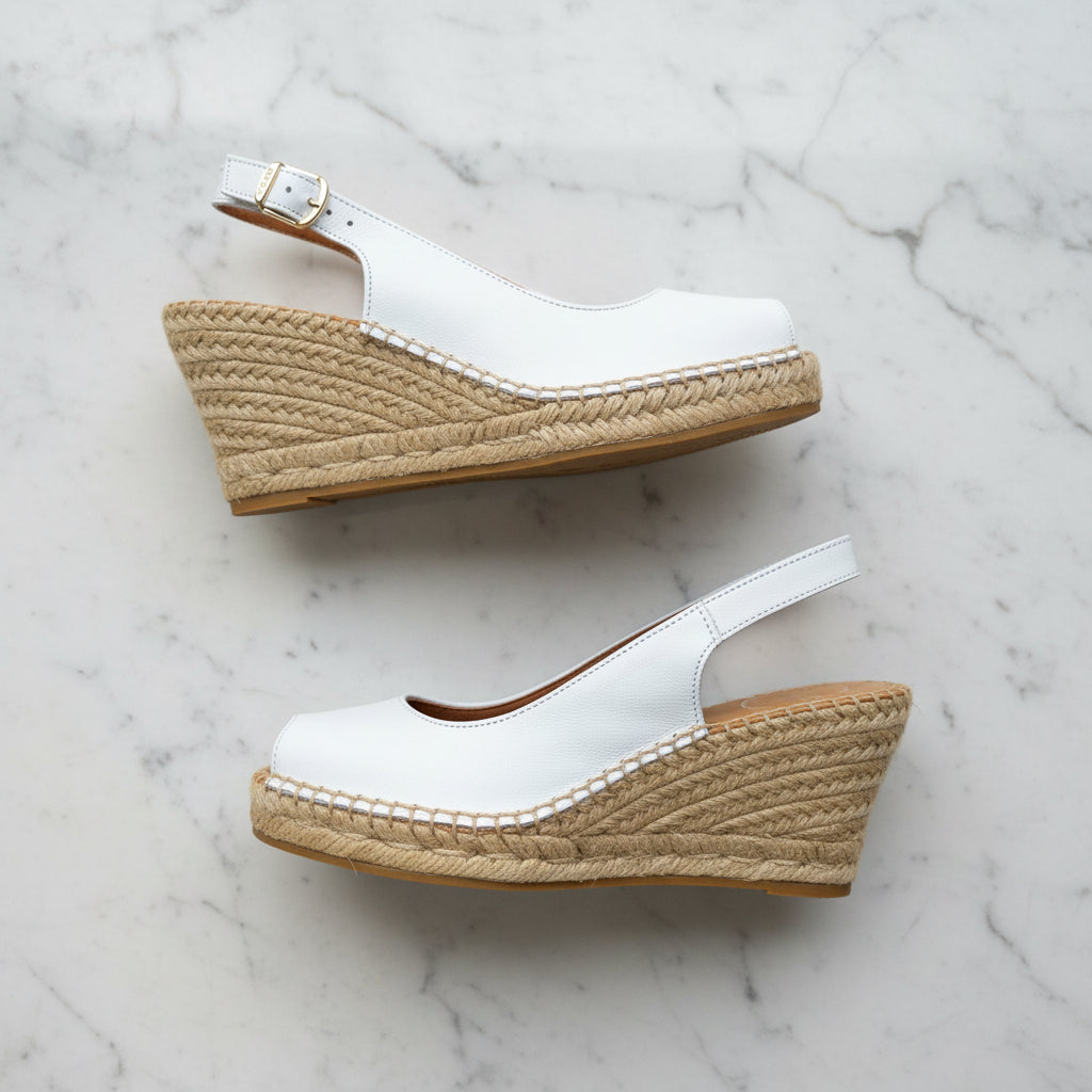 White wedge sandals with jute sole on a marble background