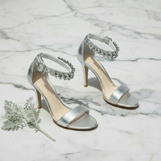Silver high-heeled sandals with embellishments on a light gray background