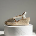Beige wedge sandal with jute sole on a white marble pedestal against a gray background