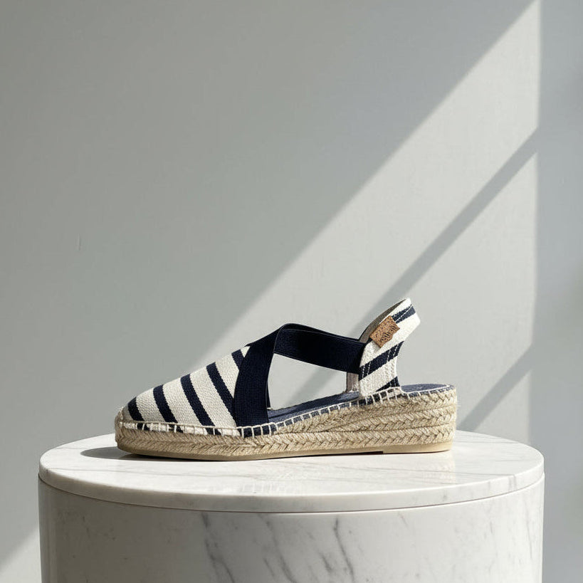 Navy and white striped sandal on a marble pedestal with a gray background