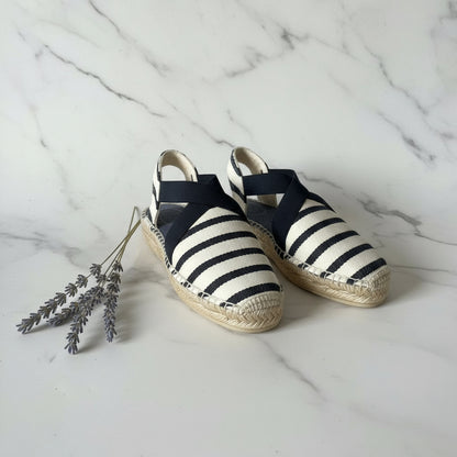 Pair of navy and white striped espadrilles on a marble surface with lavender flowers.