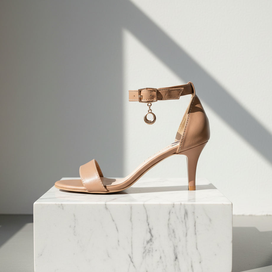 Beige high-heeled sandal with a decorative strap on a marble pedestal against a light gray background