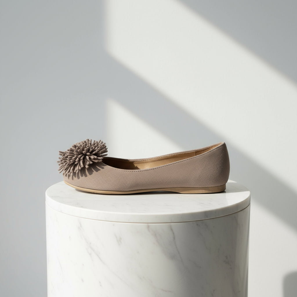 Taupe flat shoe with a pom-pom on a white background