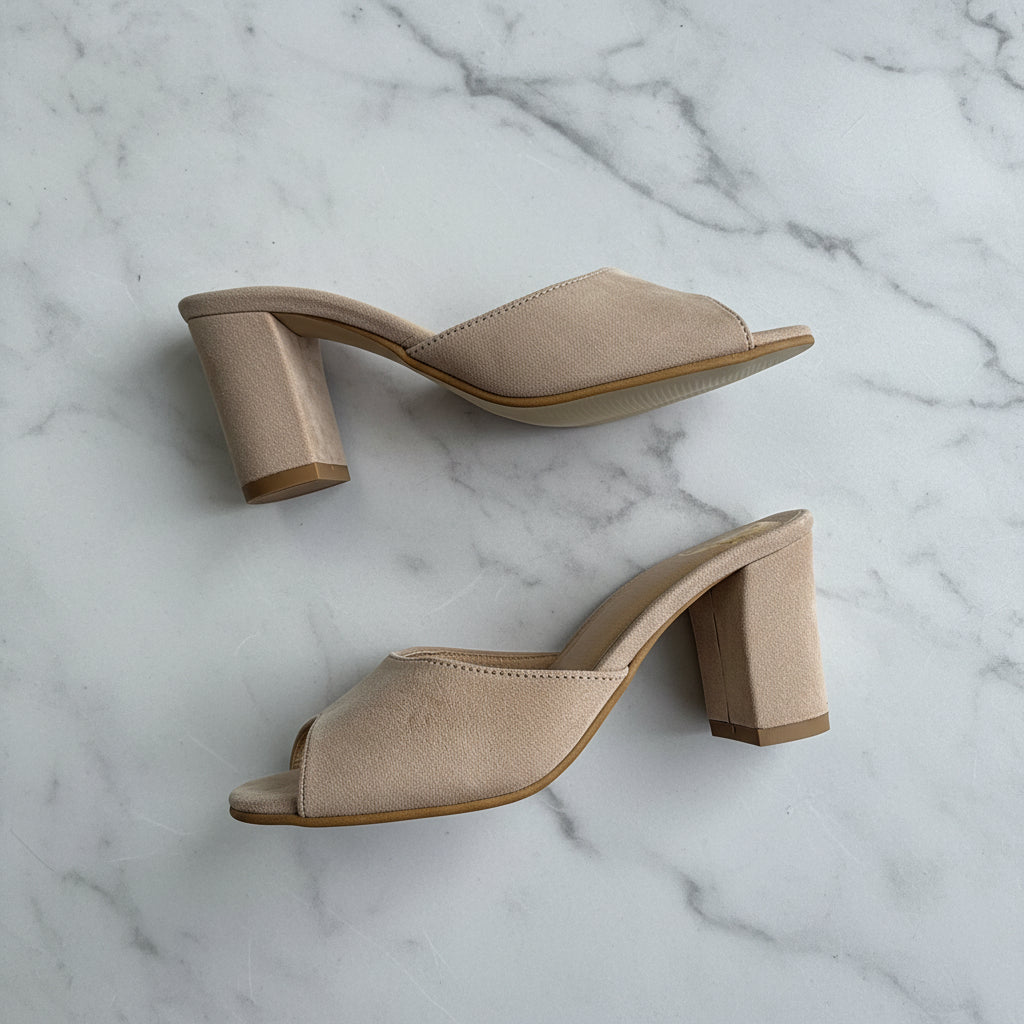 Pair of beige suede mules on a light gray background