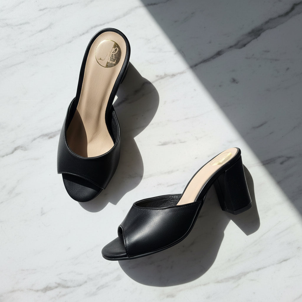 Black leather peep toe high heel mules on a white and grey marble