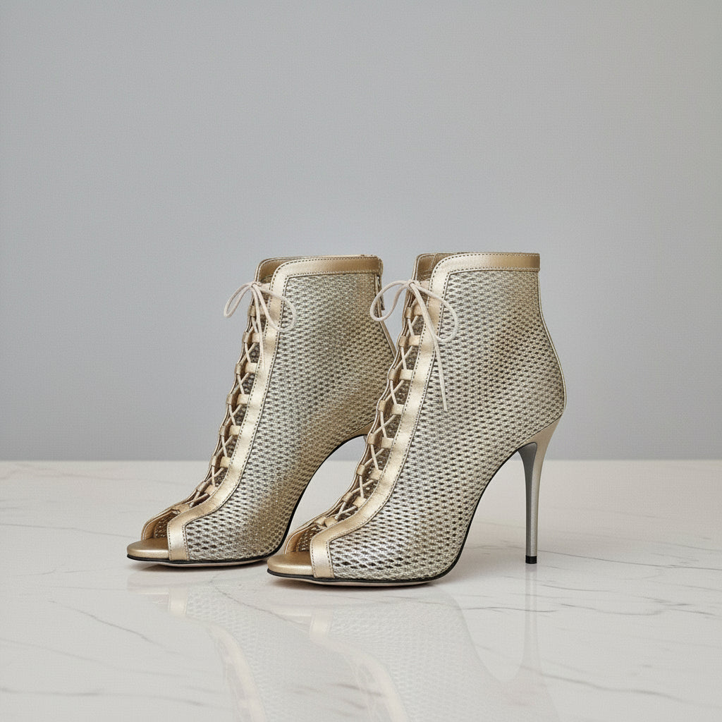Pair of VENUS gold perforated lace-up boots on marble, showing stiletto heels and 1cm platform.