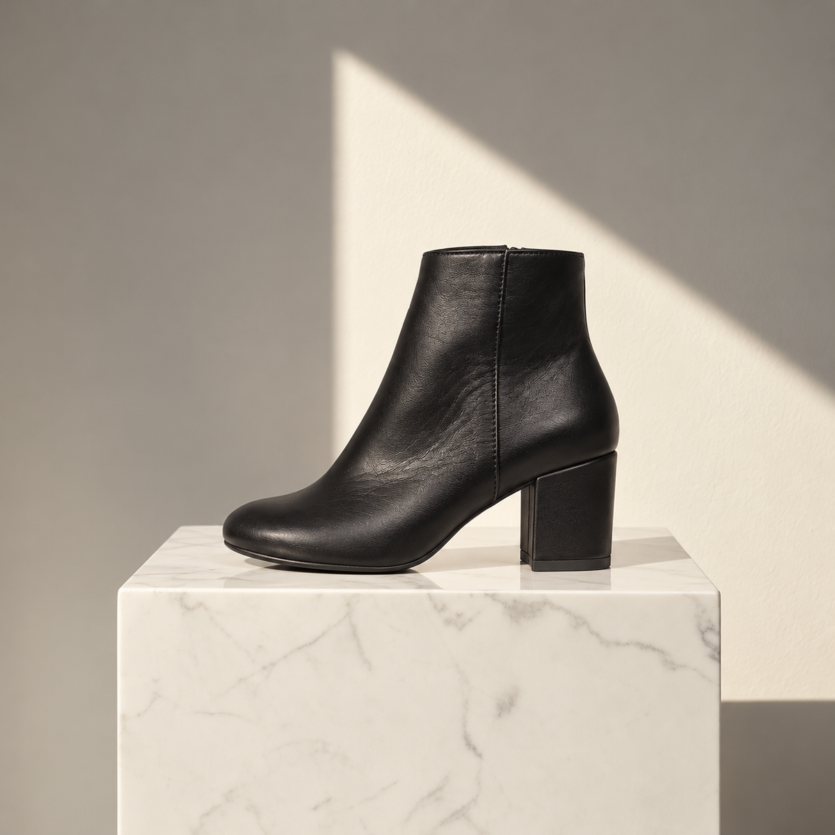 VERDE black leather ankle boot with a block heel and rounded toe, displayed in side profile on a white marble pedestal.