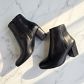 Pair of black leather almond toe ankle boots with a side zip fastening and a block heel, set on a marble surface. 