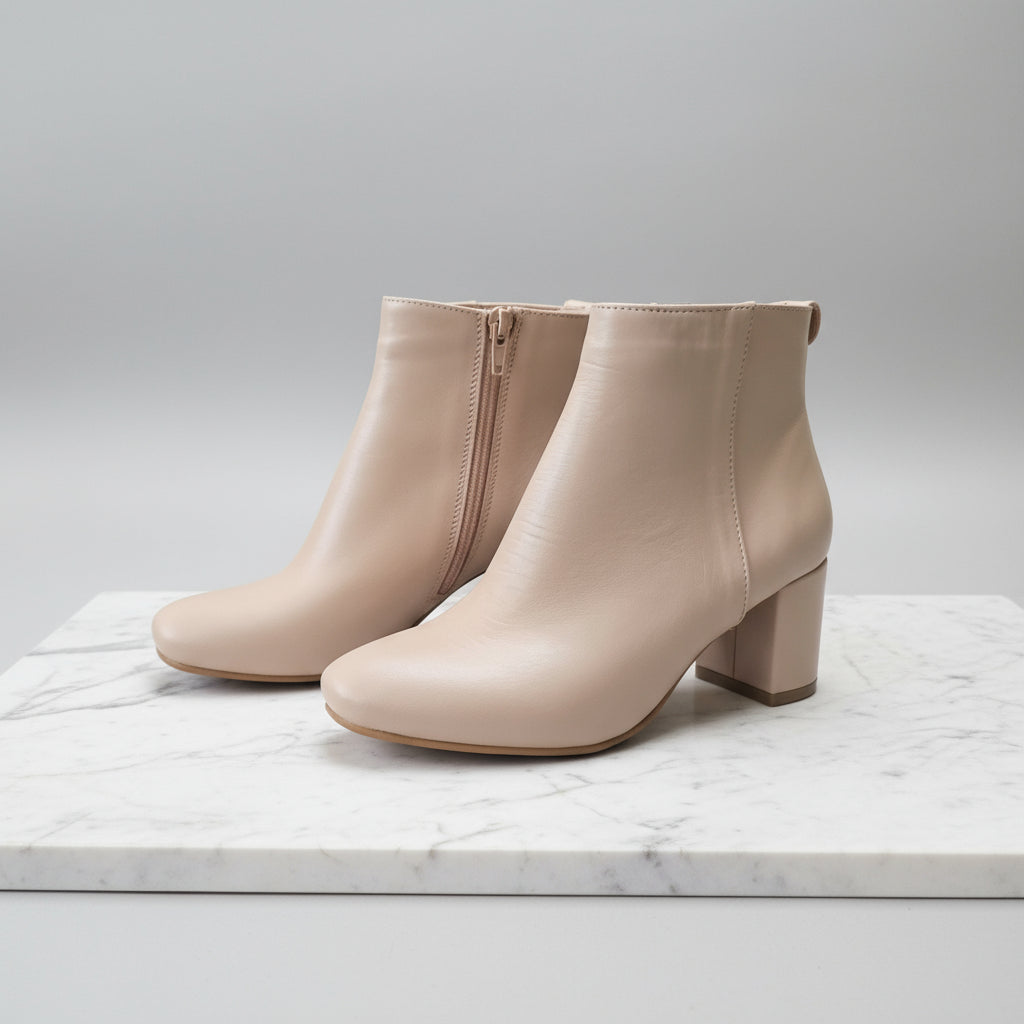 Pair of beige ankle boots on a marble surface with a light gray background