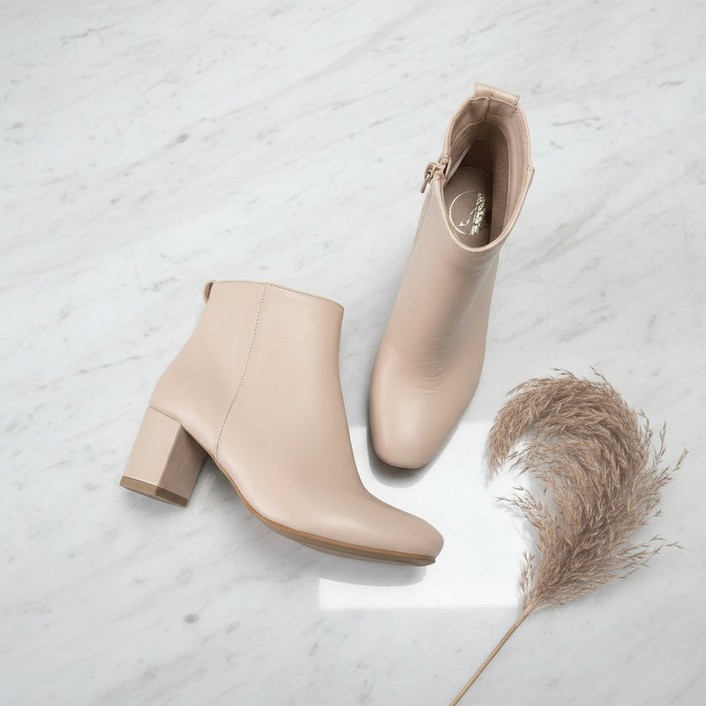Pair of beige ankle boots on a light gray surface with a dried plant for scale.