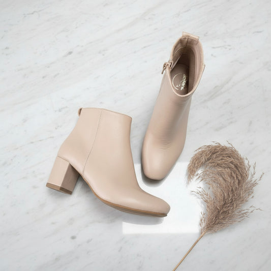 Pair of beige ankle boots on a light gray surface with a dried plant for scale.