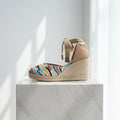 Woven wedge sandal with colorful striped design on a white marble surface.