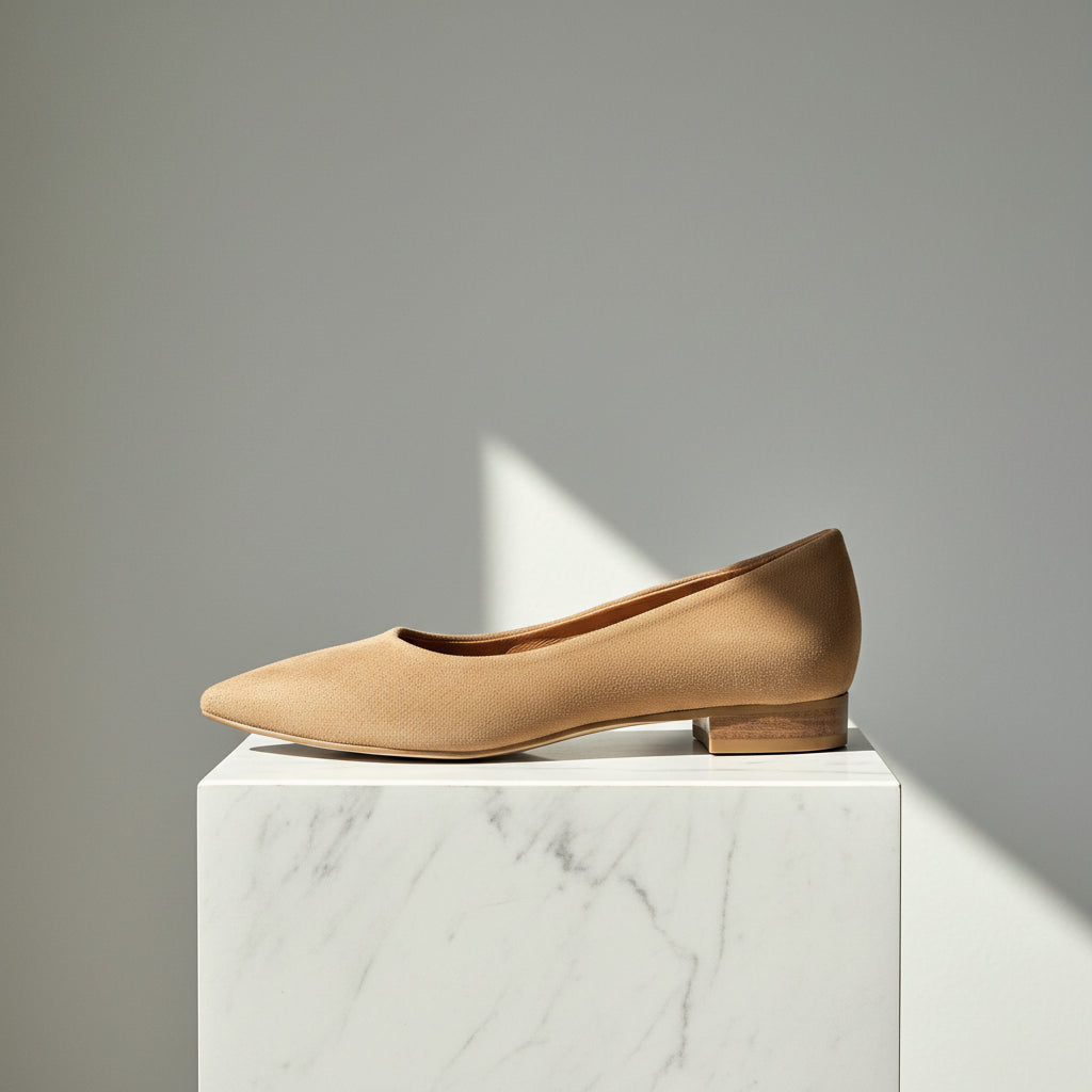 Tan flat shoe on a white marble block with a gray background