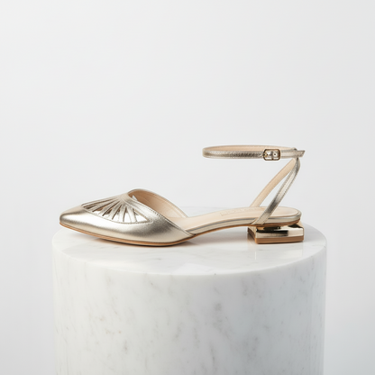 Gold leather sandal with gold strap on a white pedestal