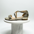 Gold sandal on a white marble pedestal against a light gray background