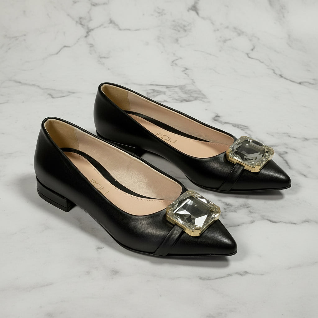 Black pointed-toe shoes with crystal embellishments on a marble surface