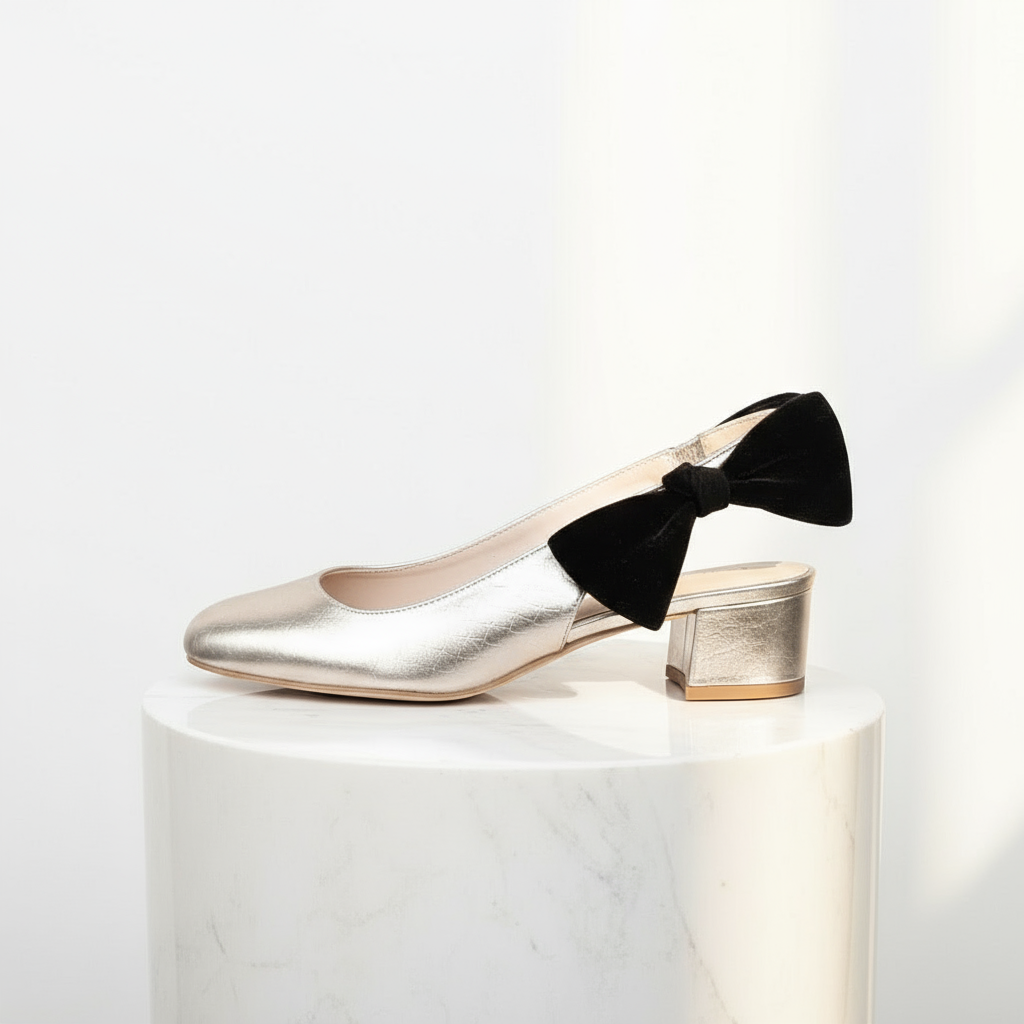 A gold leather slingback shoe with a bow detail on the ankle, displayed on a marble surface.