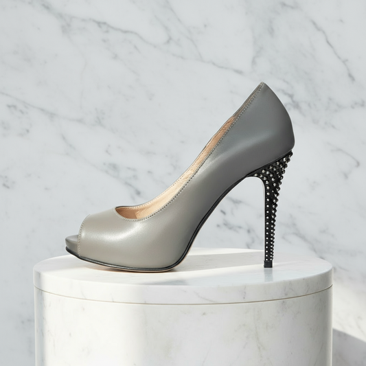 Gray high-heeled shoe with studded heel on a white pedestal against a marble background