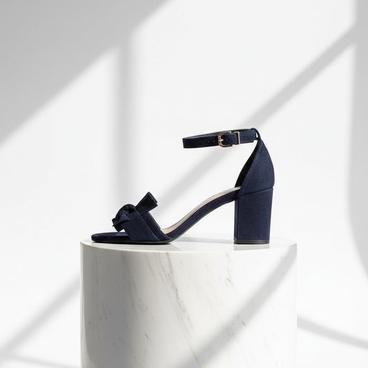 Navy blue sandal with a block heel on a white pedestal against a light background