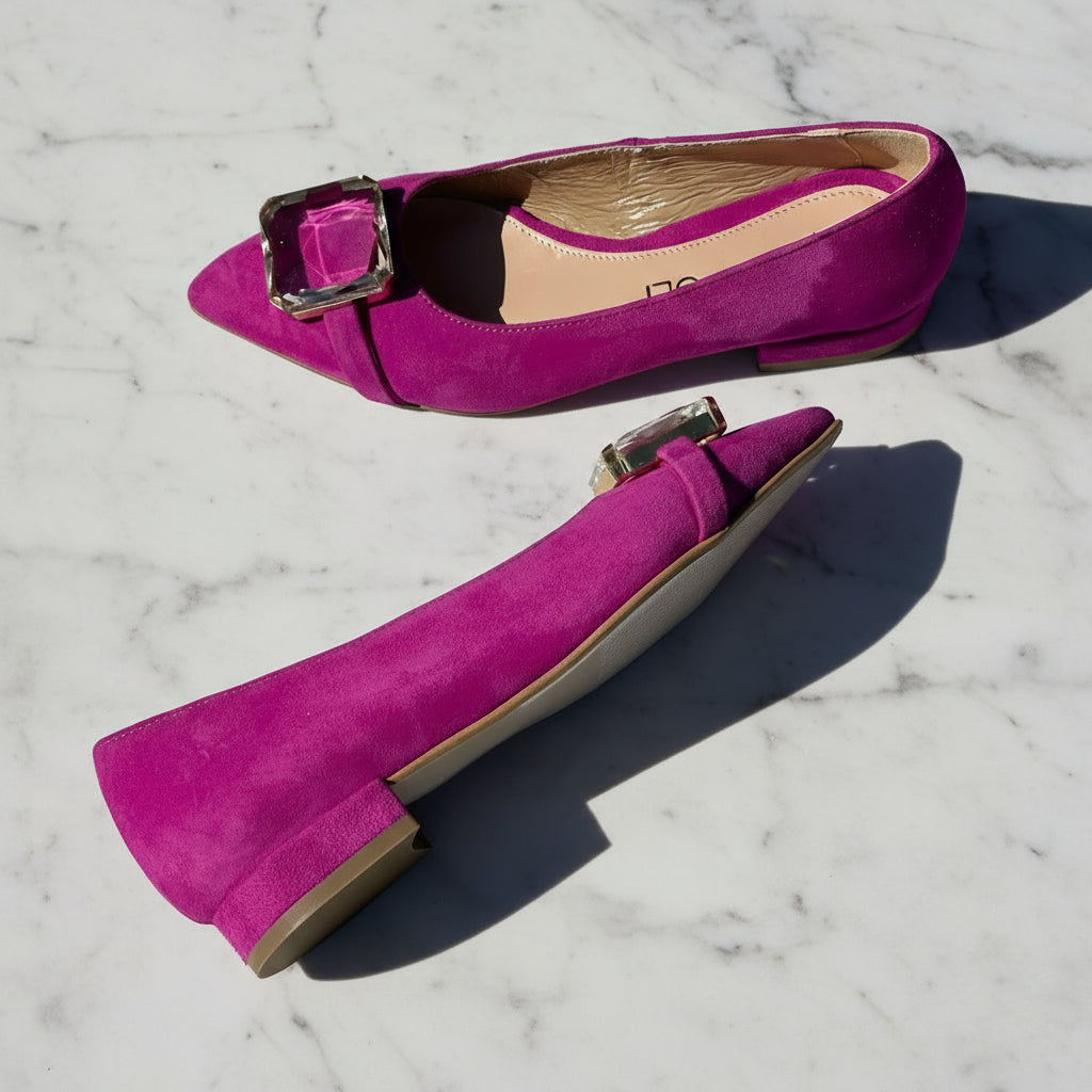 Pair of bright pink suede shoes with buckles on a marble surface