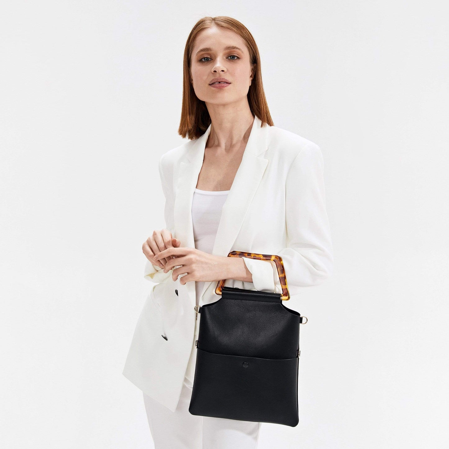 A woman in a white suite with a black handbag.